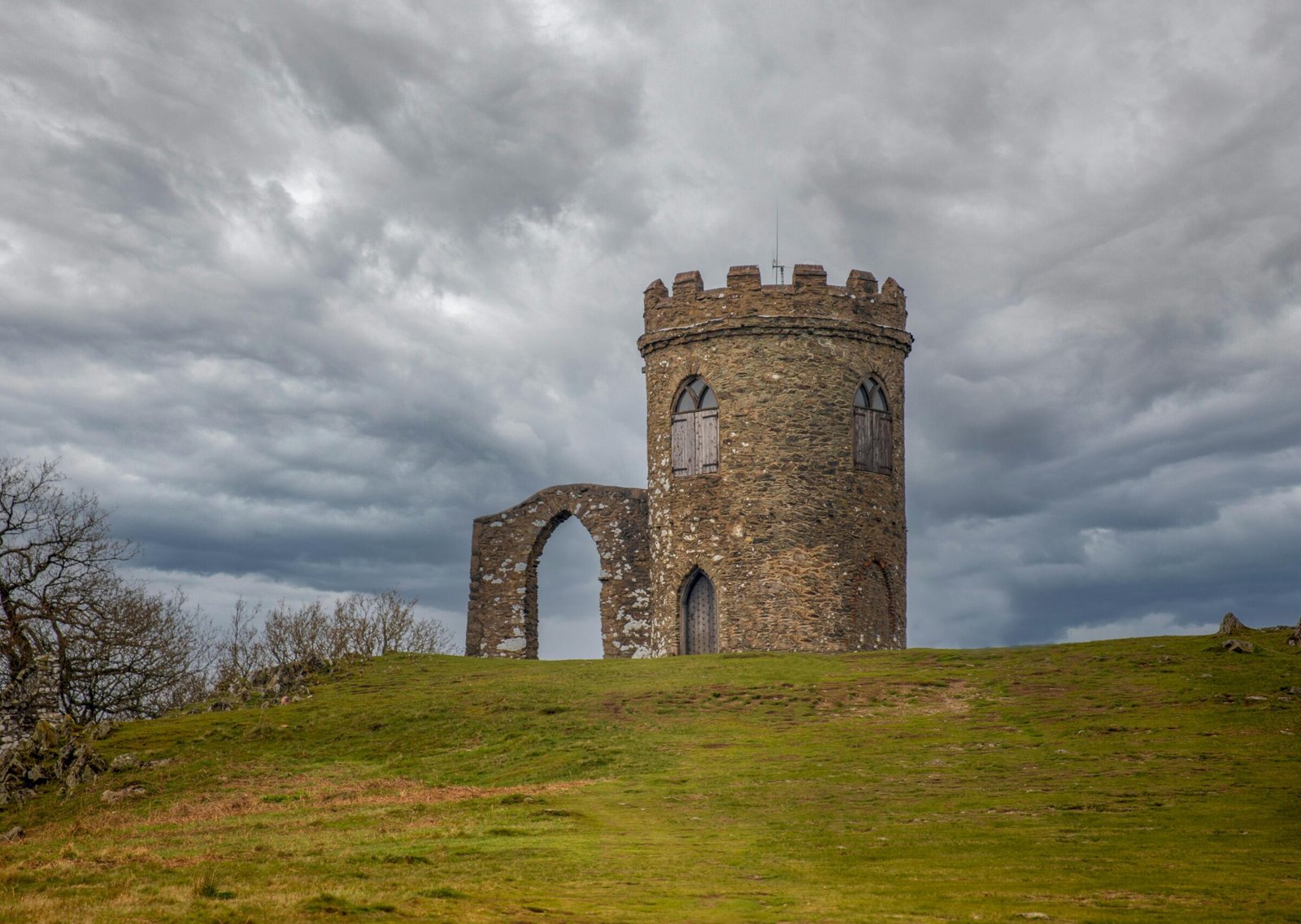 A medieval tower on a grassy hilltop in Bradgate Park, Leicester, under a dramatic sky.