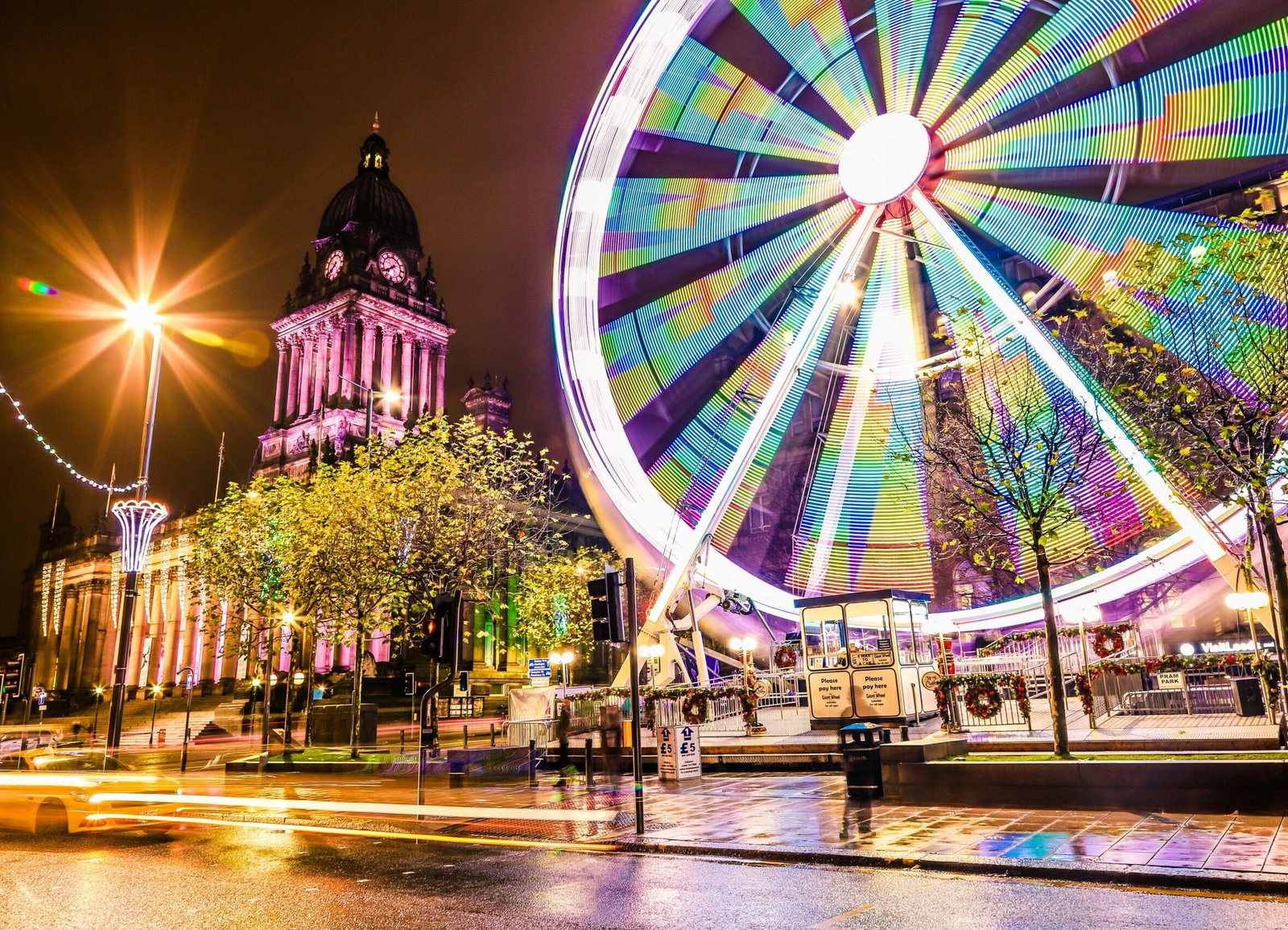 Vibrant night scene featuring Leeds Town Hall and illuminated Ferris Wheel, showcasing colorful city life.