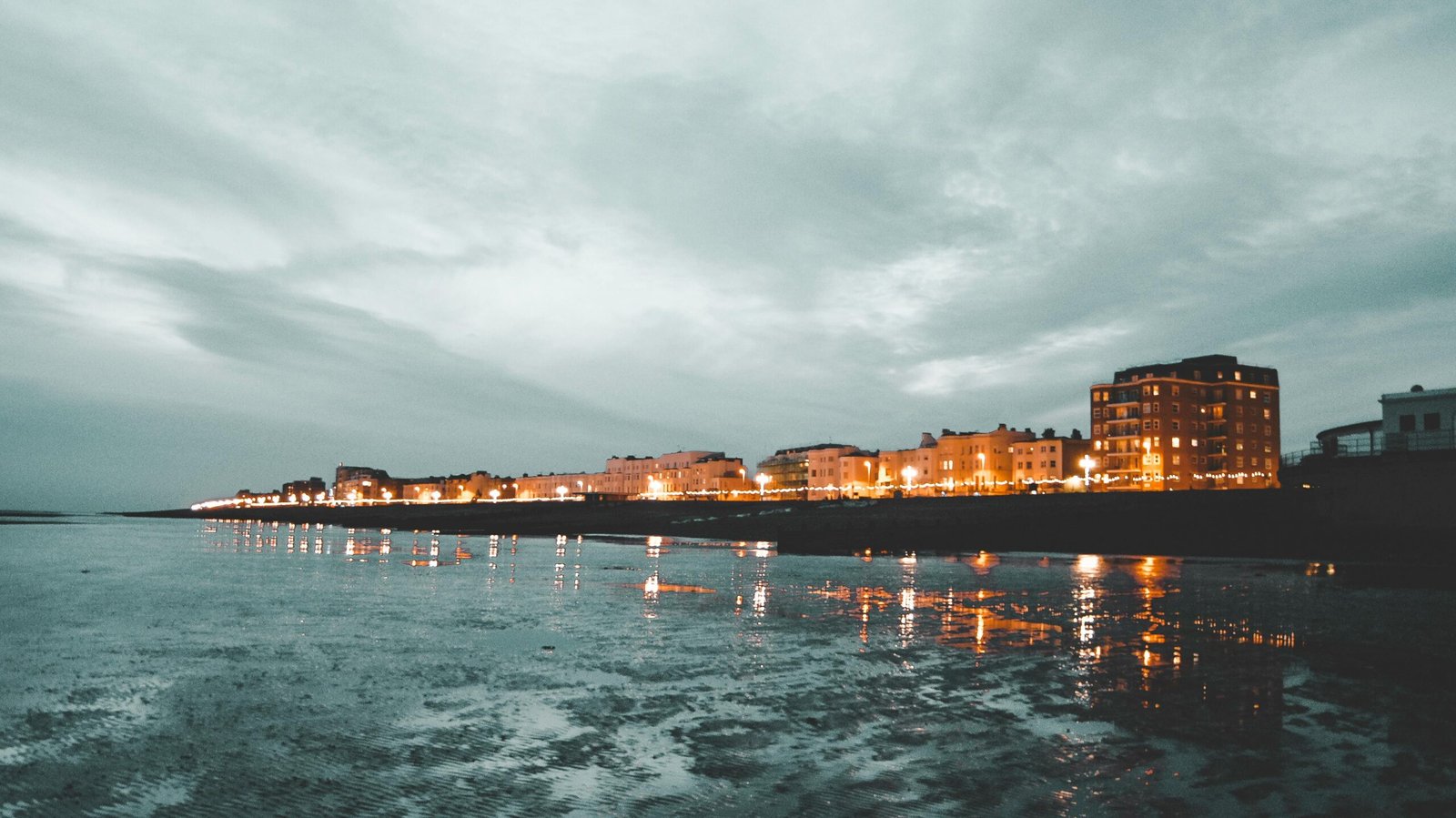 Atmospheric evening scene of the illuminated Worthing seafront reflecting on the water.